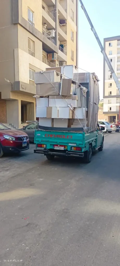 سيارة نقل عفش شركة وصال محملة بالأثاث المغلف بالكرتون أمام عمارة سكنية مع ونش هيدروليكي.